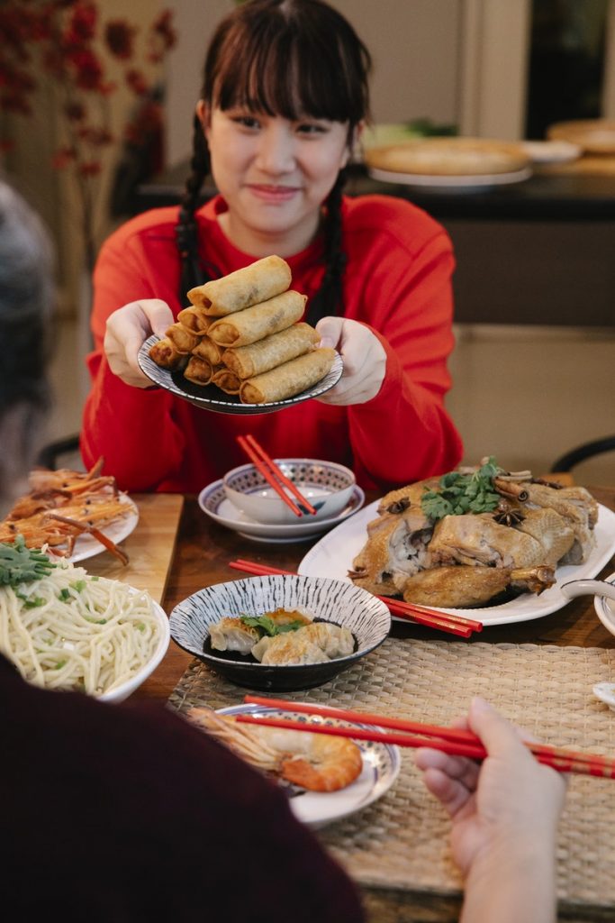 Chinese Cuisine Smiling Asian teen with spring rolls talking to crop relative